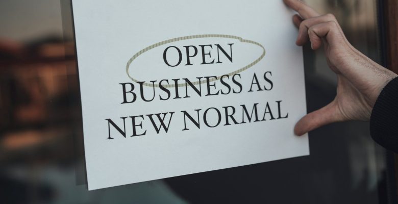a person holding a sign that says open business as new normal