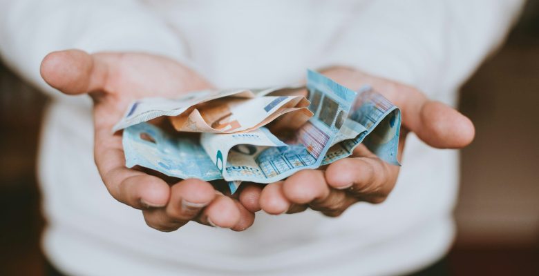 A person holding a handful of crumpled euro banknotes in their cupped hands